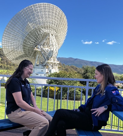 Two people smiling and chatting in front of a radio telescope.