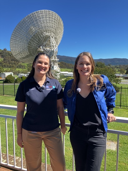 Two women standing in front of a radio telescope and smiling at the camera. 